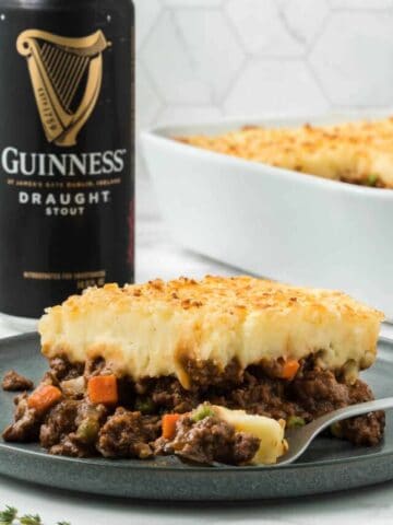 A slice of shepherd's pie with Guinness on a grey plate with a can of Guinness beer in the background.