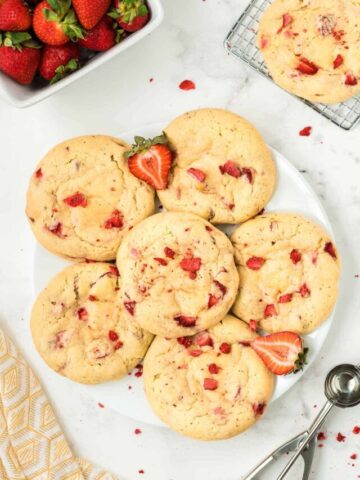 Strawberry cheesecake cookies stacked on a white plate with freeze-dried strawberries sprinkled around.