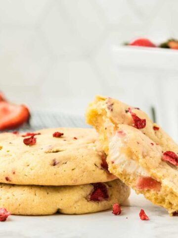 Two strawberry cheesecake cookies stacked with a third cookie showing the cheesecake filling.