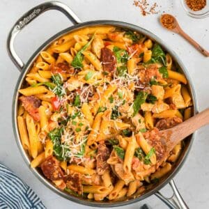 Chicken and chorizo pasta with a wooden spoon in a stainless steel pan.
