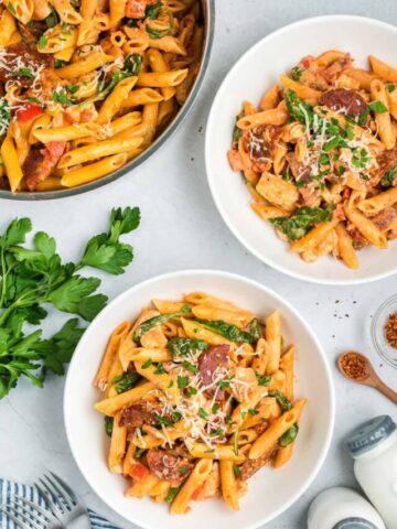 Two bowls of chicken and chorizo pasta alongside a pan of pasta.