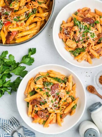 Two bowls of chicken and chorizo pasta alongside a pan of pasta.