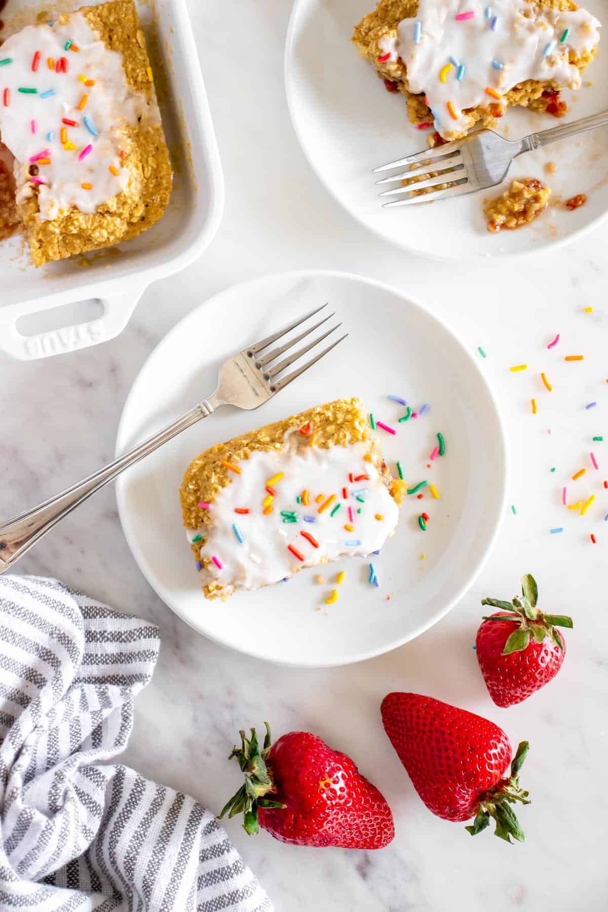 Strawberry pop tart baked oats with frosting and sprinkles served on a white plate.