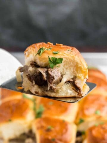 A philly cheesesteak slider lifted above other sliders.