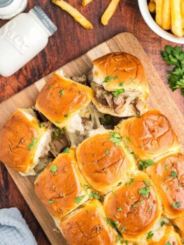 Philly cheesesteak sliders topped with fresh parsley and served with french fries.