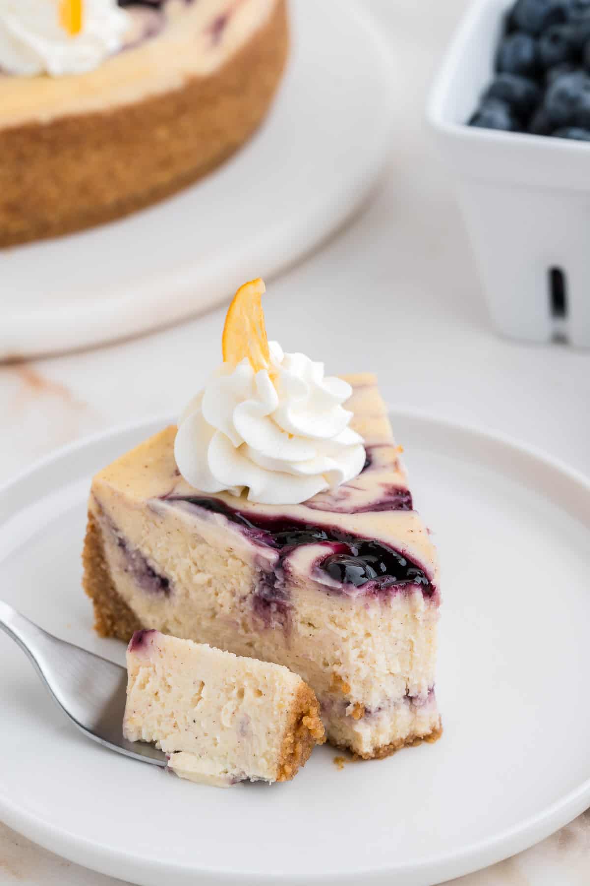 A slice of lemon blueberry cheesecake with a bite taken out.