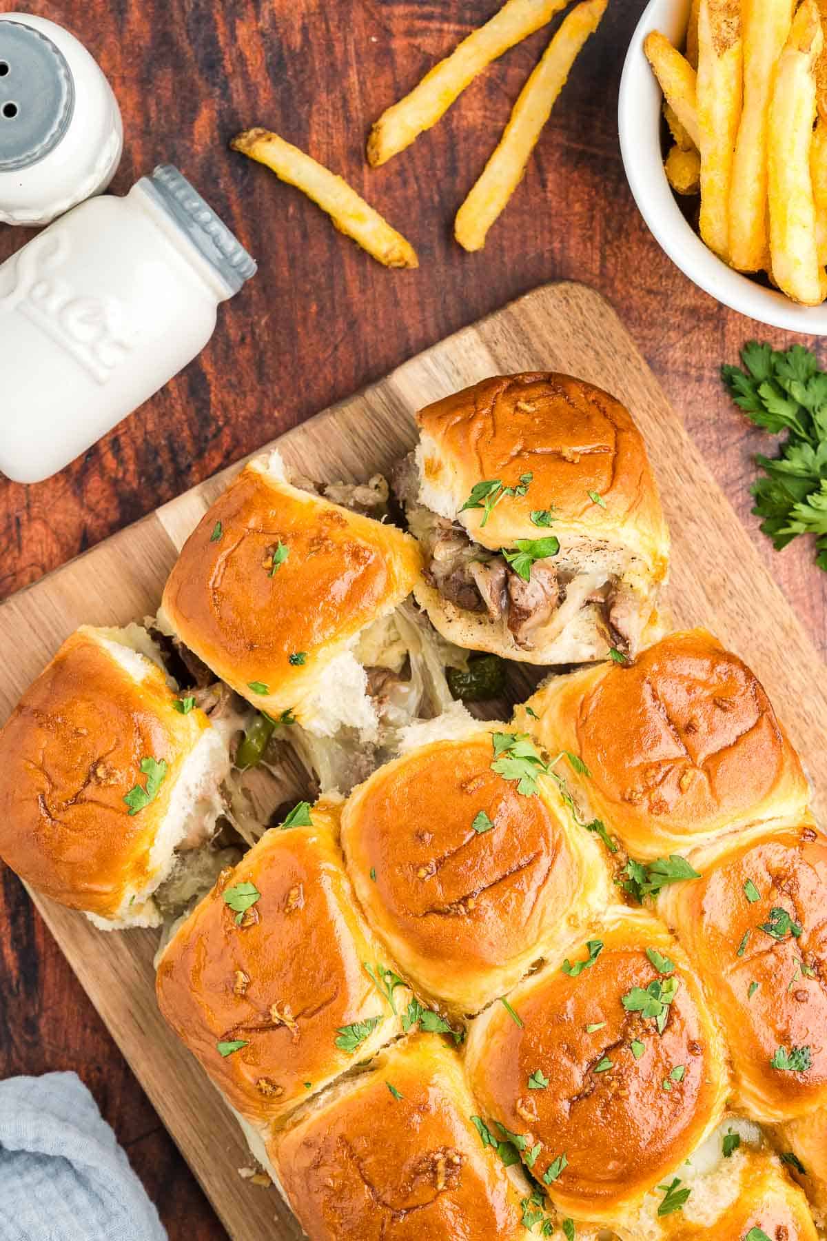 Philly cheesesteak sliders topped with fresh parsley and served with french fries.
