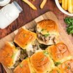 Philly cheesesteak sliders with melty provolone cheese on a wooden board.