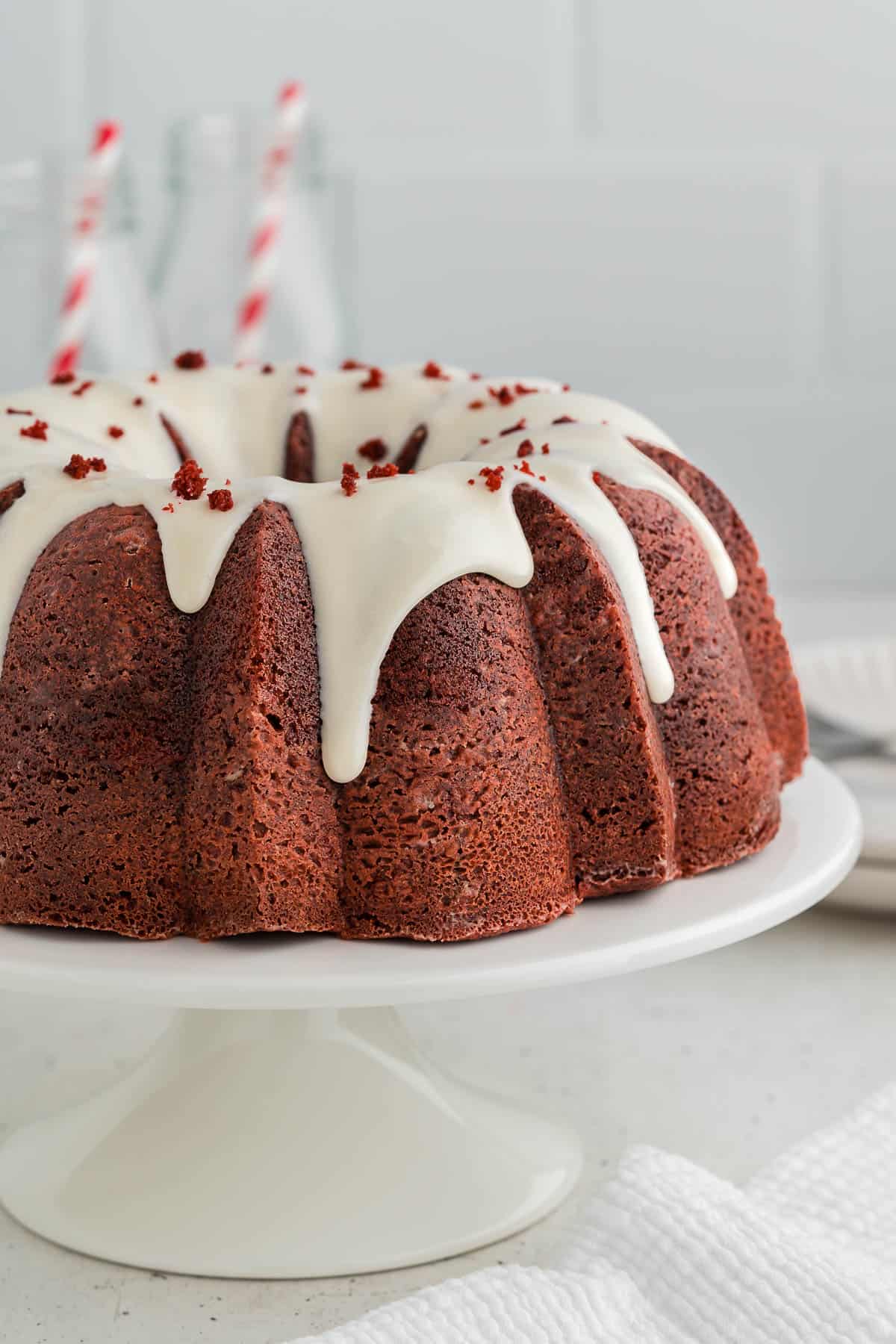 Red velvet bundt cake with cream cheese frosting on a white cake stand.