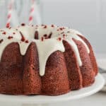 Red velvet bundt cake with cream cheese frosting served on a white cake stand.