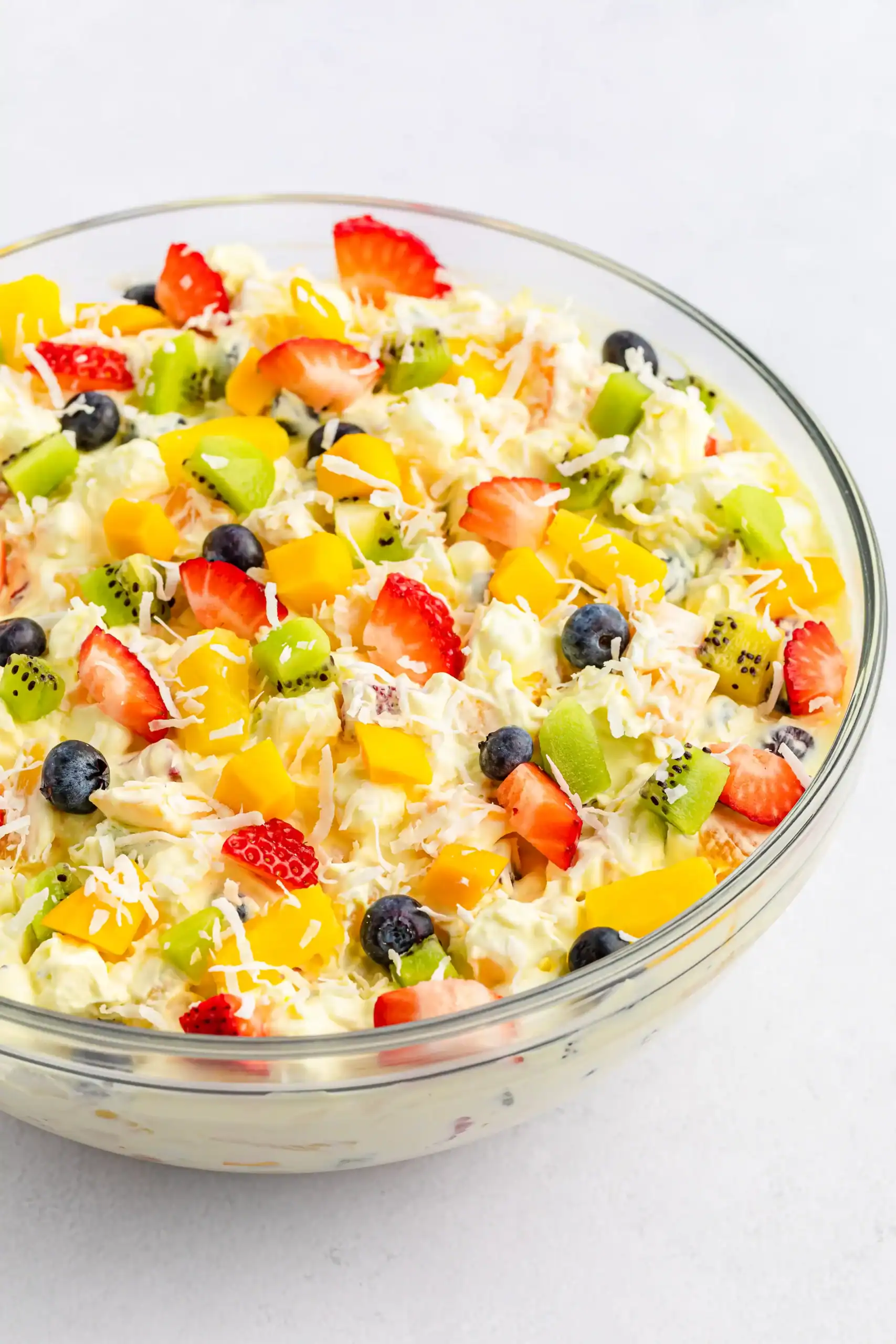 A clear glass bowl of tropical fruit fluff salad sprinkled with shredded coconut.
