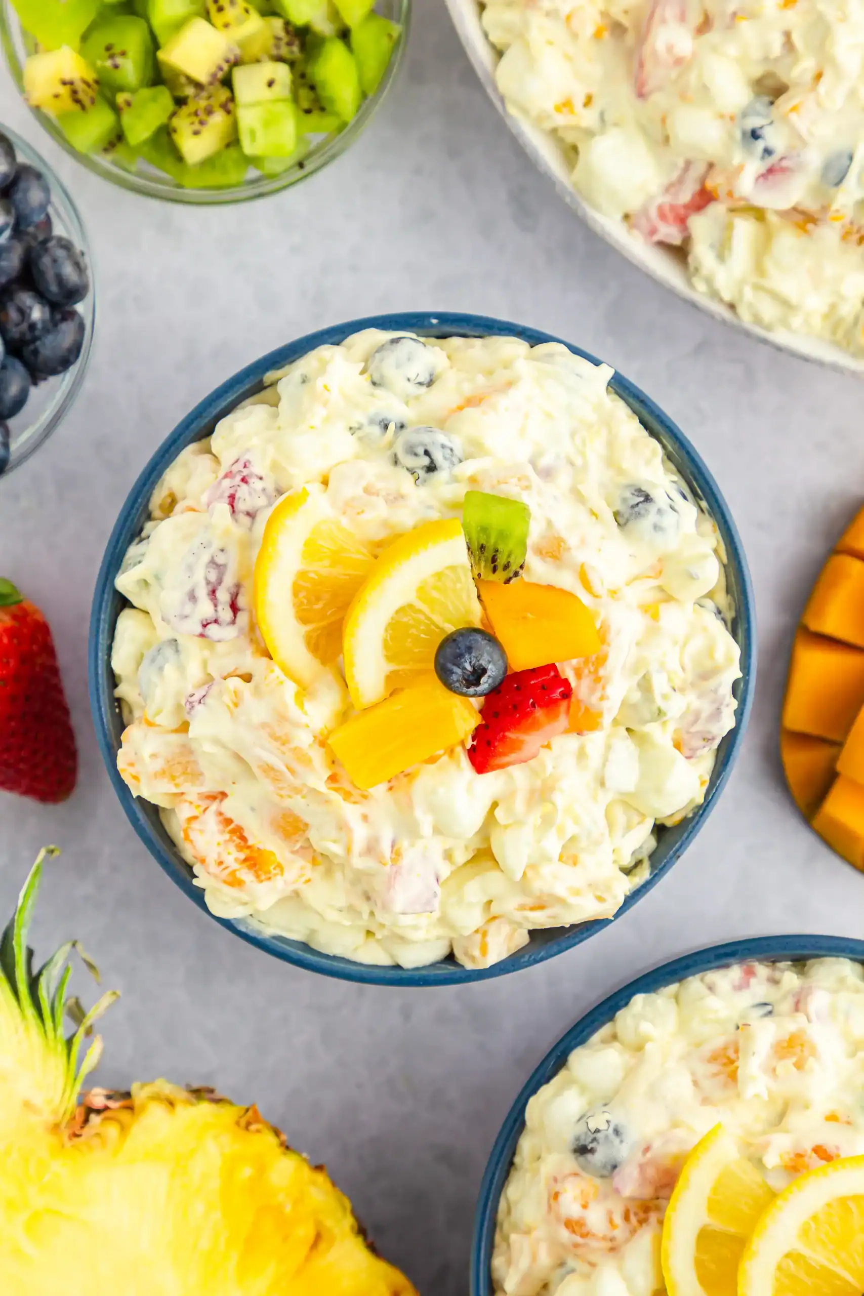 An overhead of tropical fluff salad with a cut pineapple, kiwi, strawberries, and mango in the shot.
