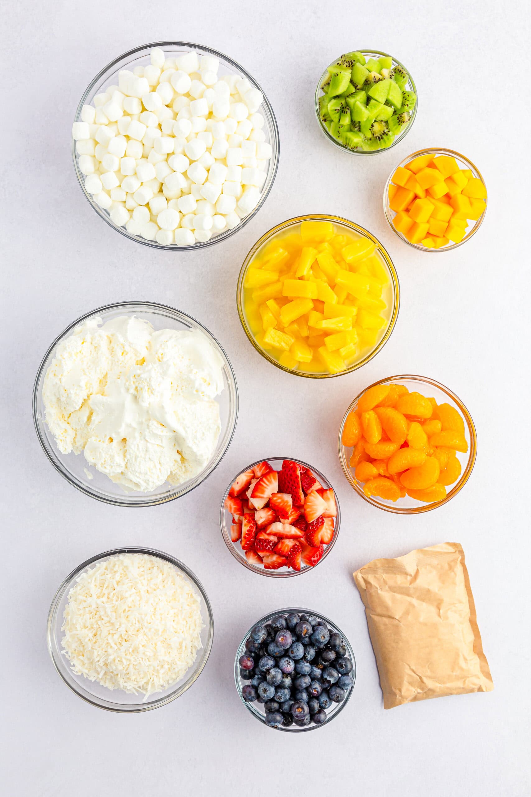 Ingredients for tropical fruit fluff salad in individual glass mixing bowls.