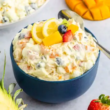 A navy blue bowl of tropical fruit fluff salad with a spoon and chopped fruit.