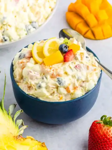 A navy blue bowl of tropical fruit fluff salad with a spoon and chopped fruit.