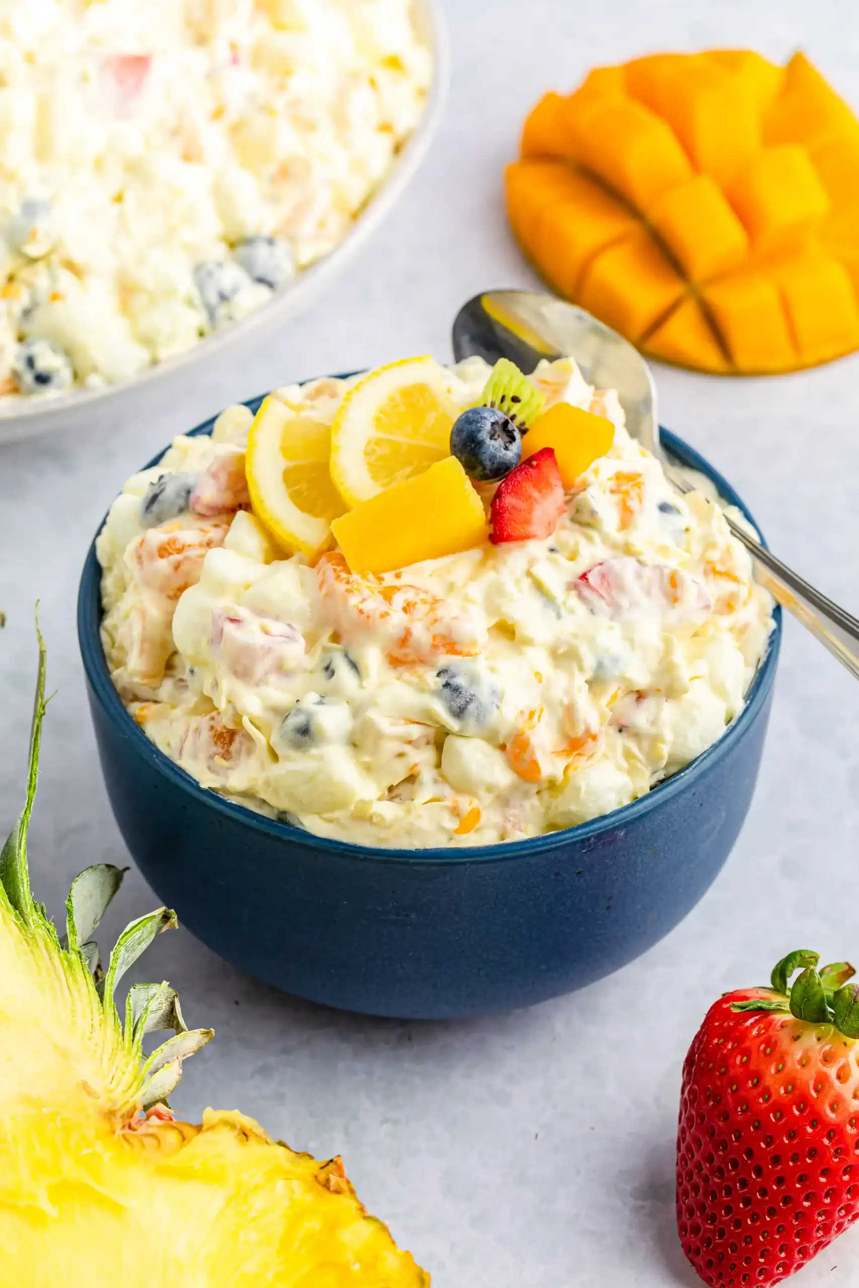 A navy blue bowl of tropical fruit fluff salad with a spoon and chopped fruit.
