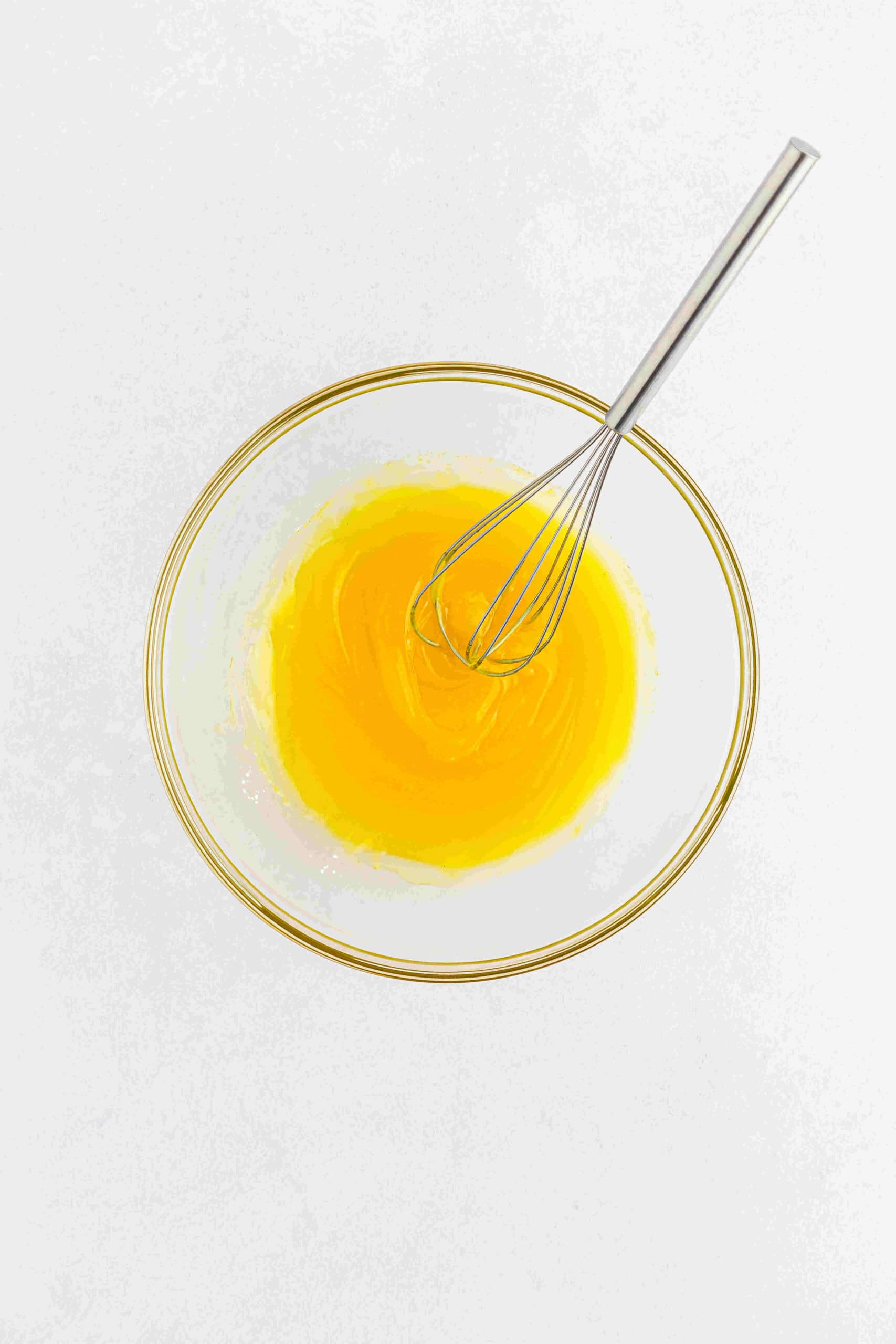 Pineapple juice and lemon jello pudding mixed together with a whisk in a glass bowl.