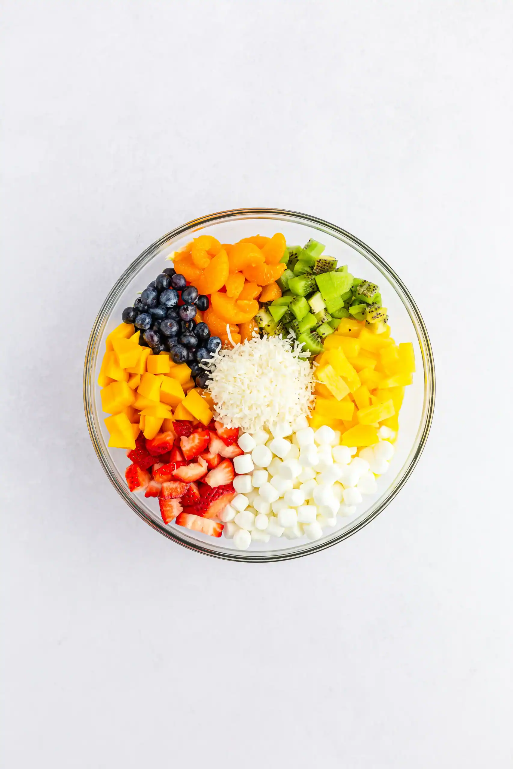 Ingredients for tropical fruit fluff salad together in a glass mixing bowl.